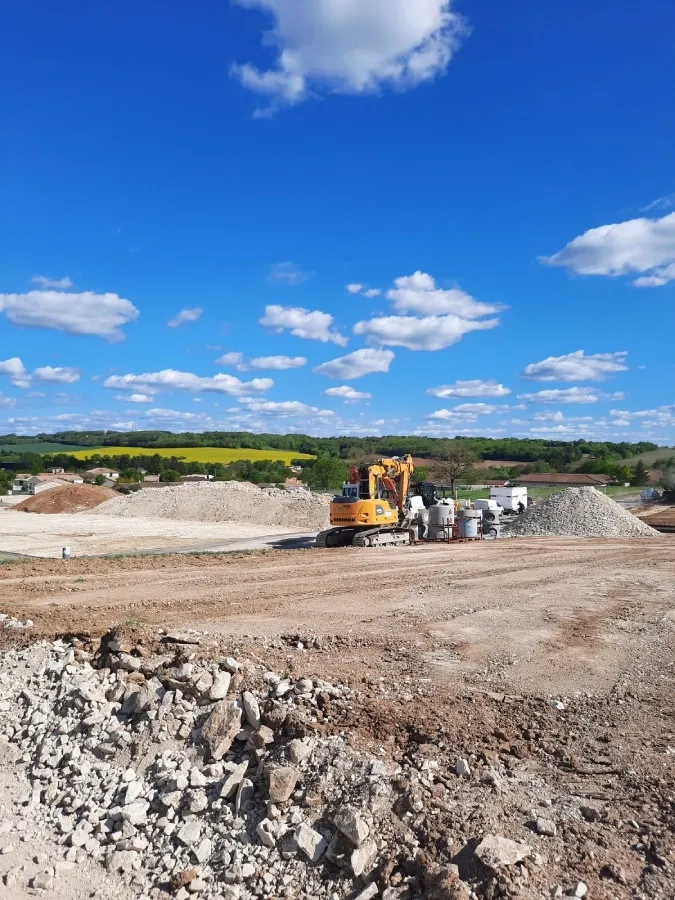 Engin de terrassement jaune sur un grand chantier de terrain décapé, avec tas de gravats