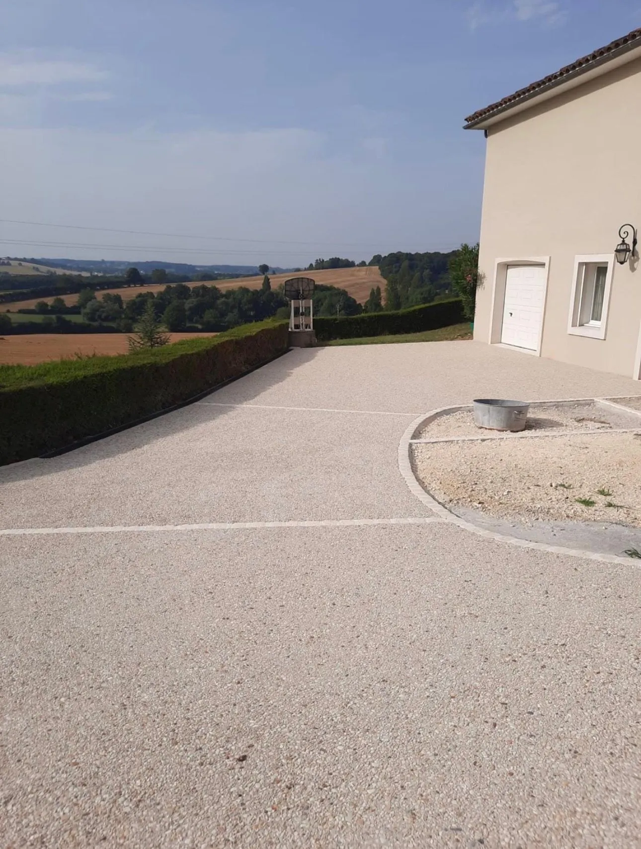 Large allée en gravillons clairs devant une maison, avec vue sur la campagne