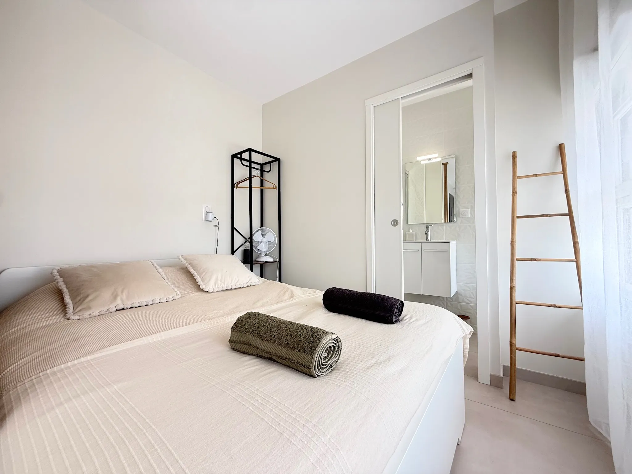 Chambre aux murs clairs, lit blanc et porte coulissante ouvrant sur la salle d'eau