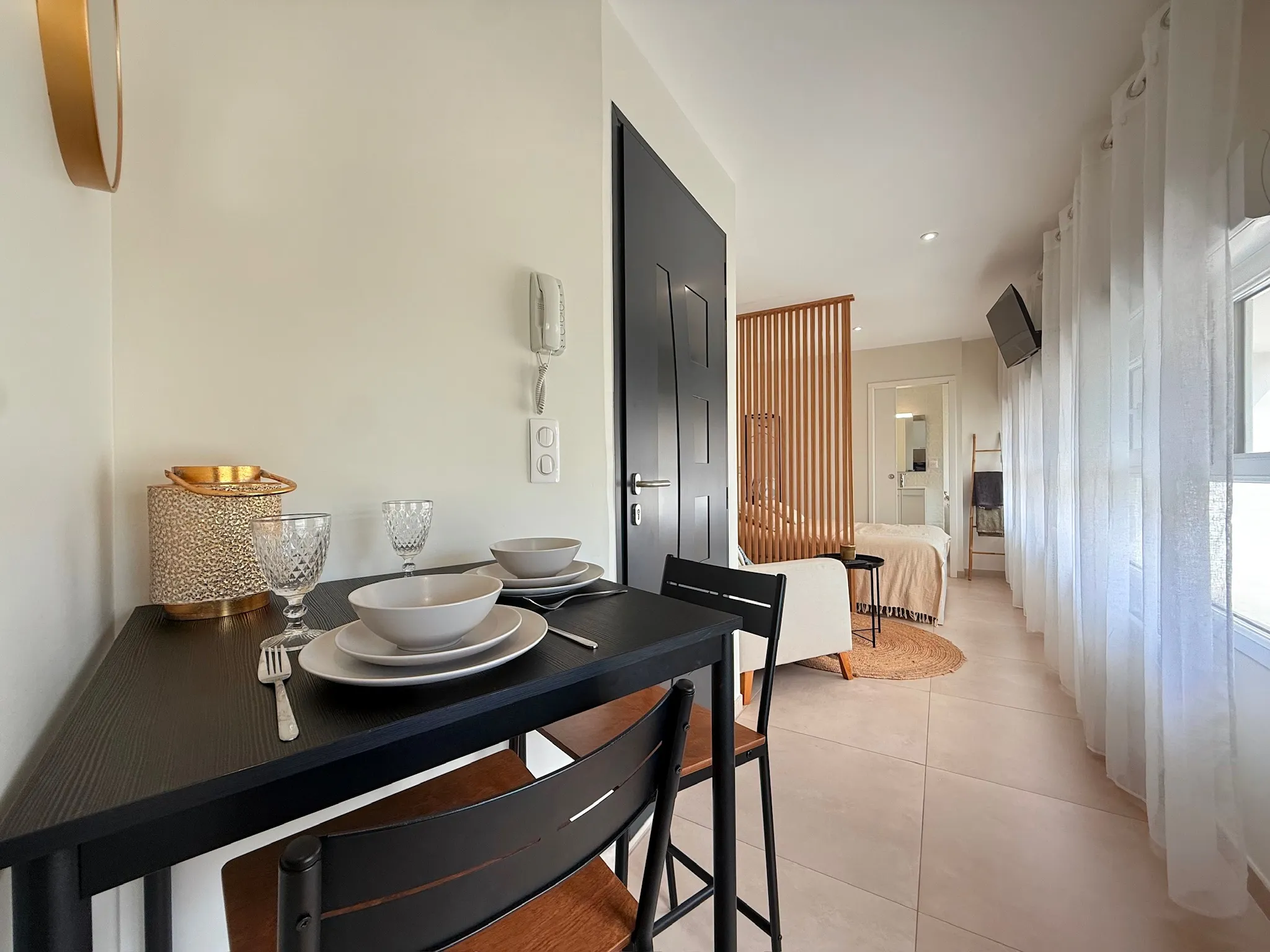 Coin repas avec table noire et deux chaises, porte anthracite et rideaux blancs devant la fenêtre
