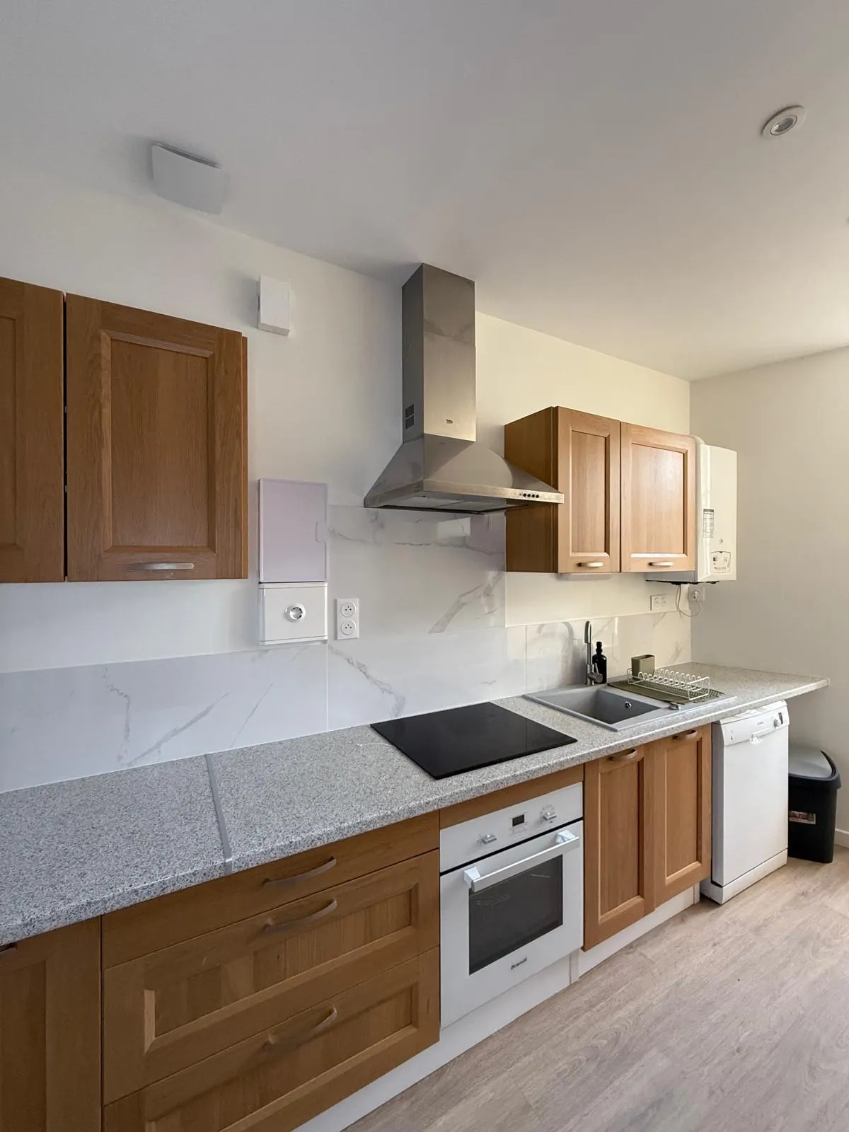 Cuisine équipée aux façades en bois, plan de travail granité gris et crédence en carreaux effet marbre