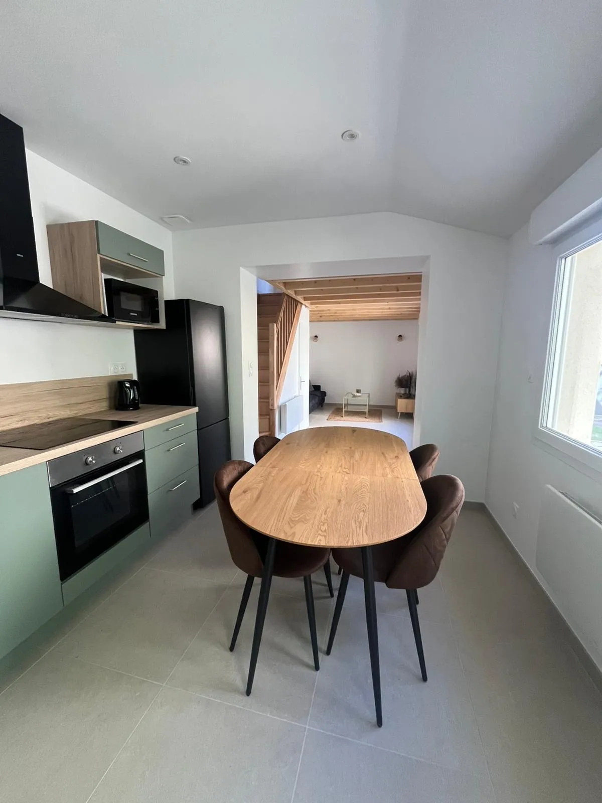 Cuisine verte et table ovale en bois, avec le séjour aux poutres apparentes en perspective