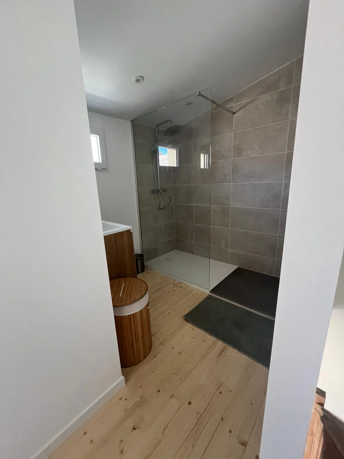 Douche à l'italienne aux murs carrelés taupe, paroi vitrée et sol en lames de bois clair