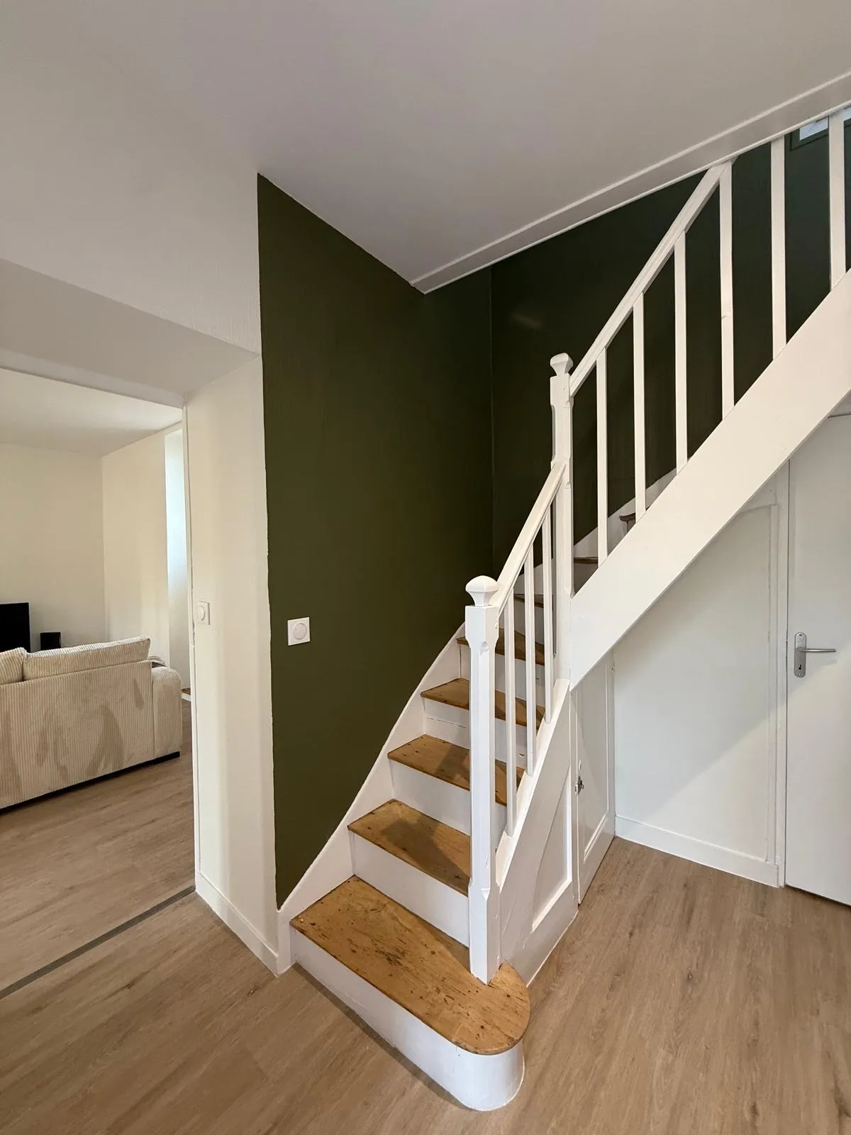 Escalier blanc aux marches en bois, contre un mur peint en vert olive
