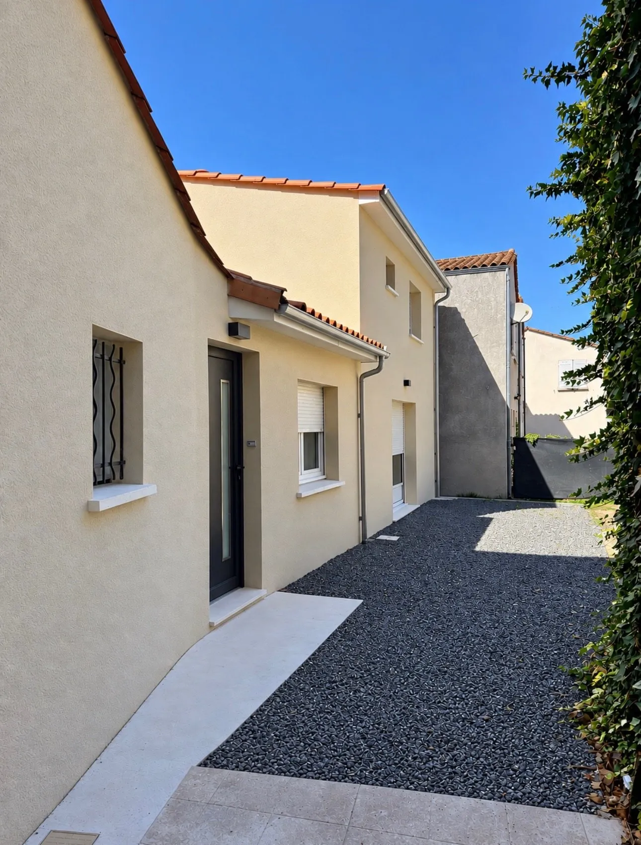 Maisons à façades enduites beiges, porte anthracite et allée en galets noirs