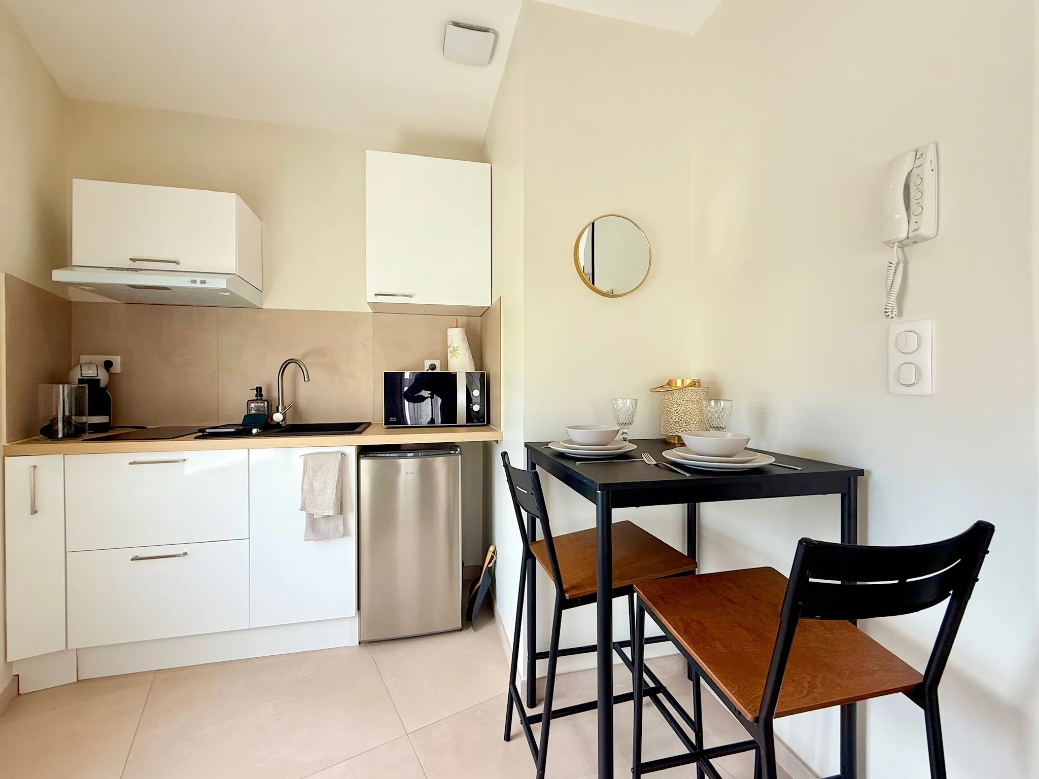 Kitchenette aux meubles blancs avec crédence beige, et petite table haute noire avec deux chaises