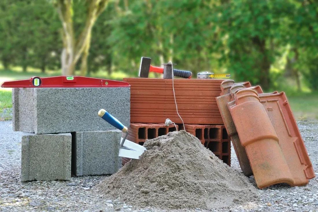 Parpaings, briques, tuiles, sable, niveau et truelle posés sur un chantier