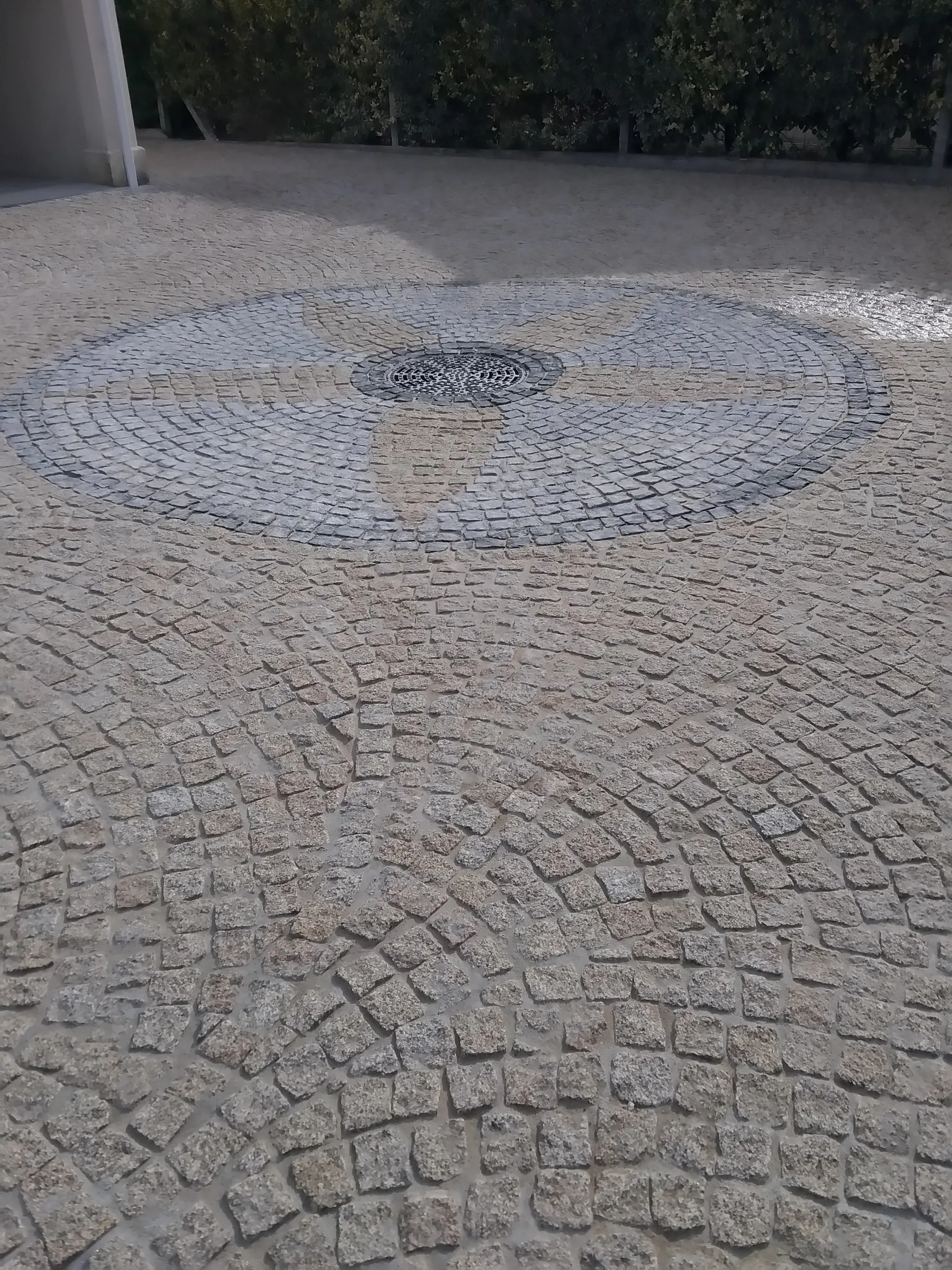 Cour pavée en granit posée en arcs de cercle autour d'un motif circulaire central avec une grille d'évacuation