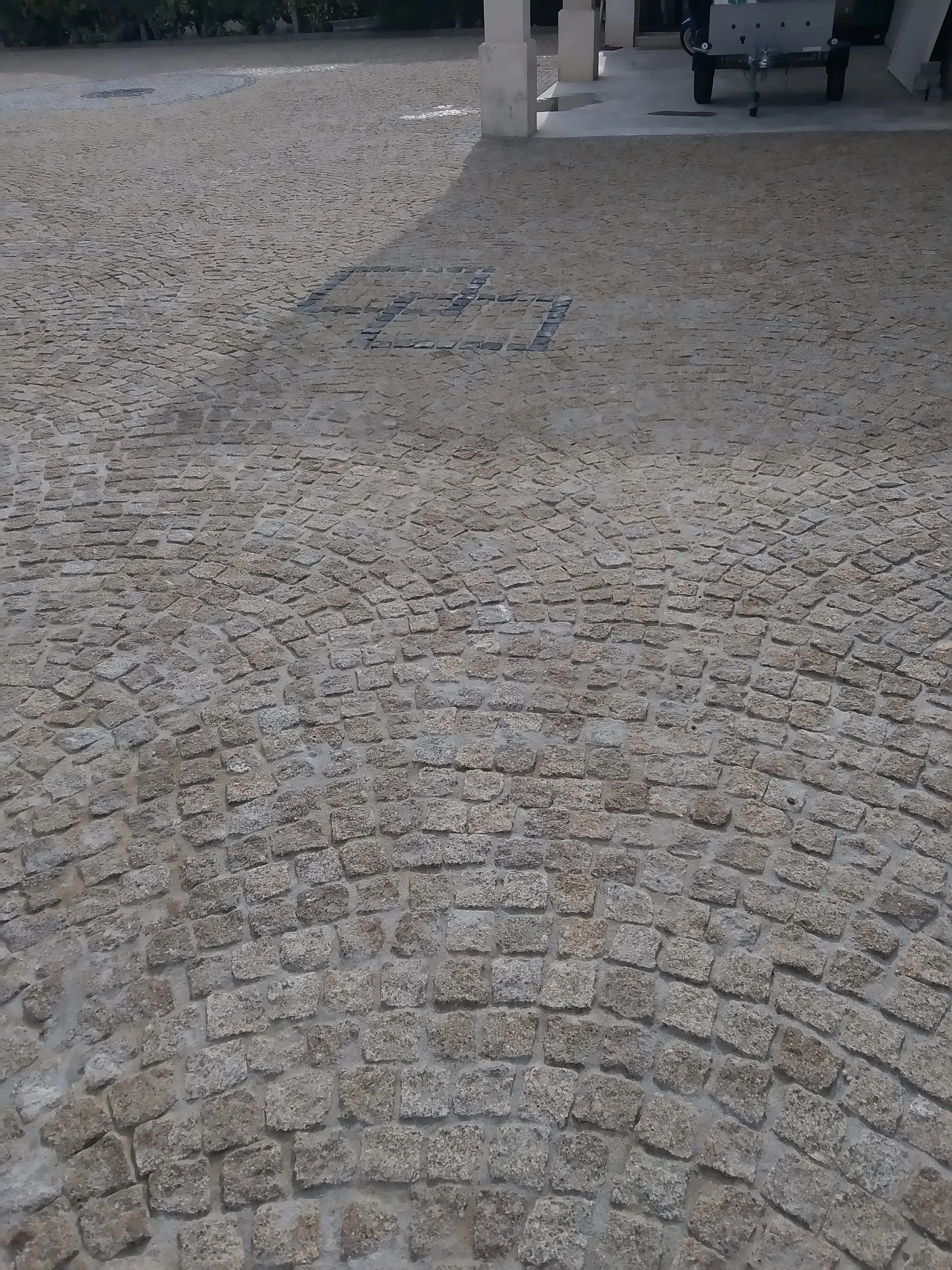 Cour pavée en granit devant un porche, avec un petit motif carré en pavés foncés
