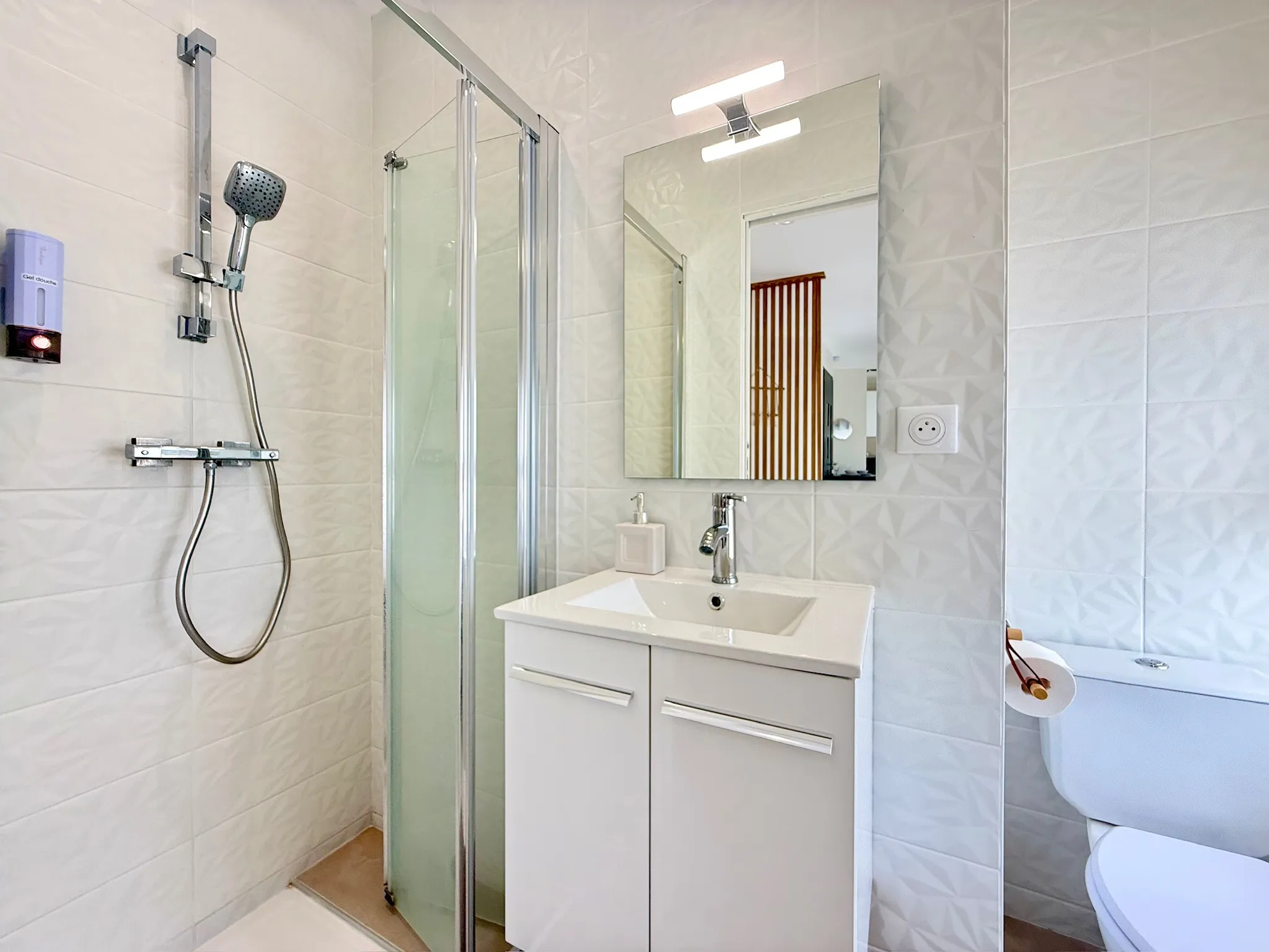Salle d'eau aux carreaux blancs en relief, douche vitrée et vasque sur meuble blanc