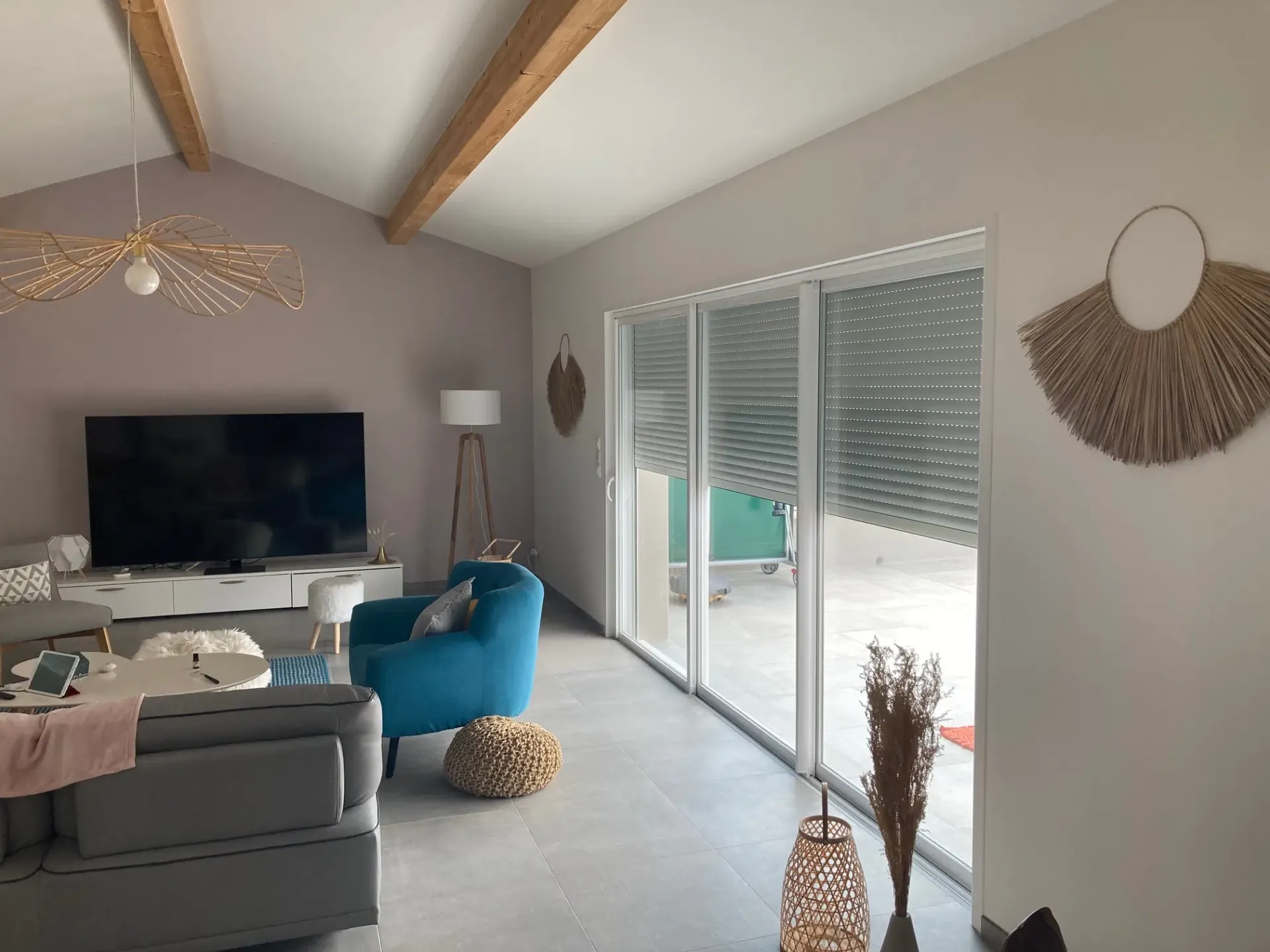 Baie vitrée coulissante à trois vantaux équipée d'un volet roulant, dans un salon aux poutres apparentes