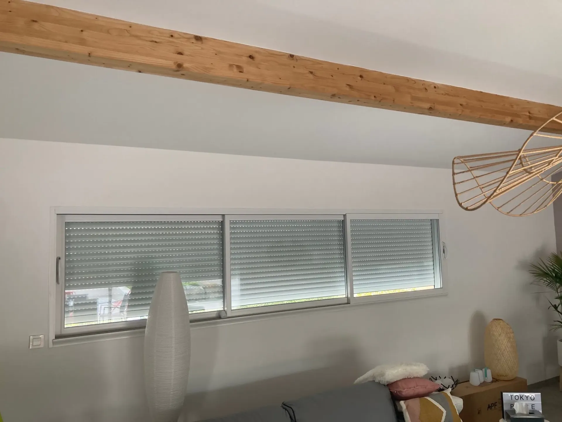 Fenêtre coulissante en bandeau avec volet roulant baissé, sous une poutre en bois