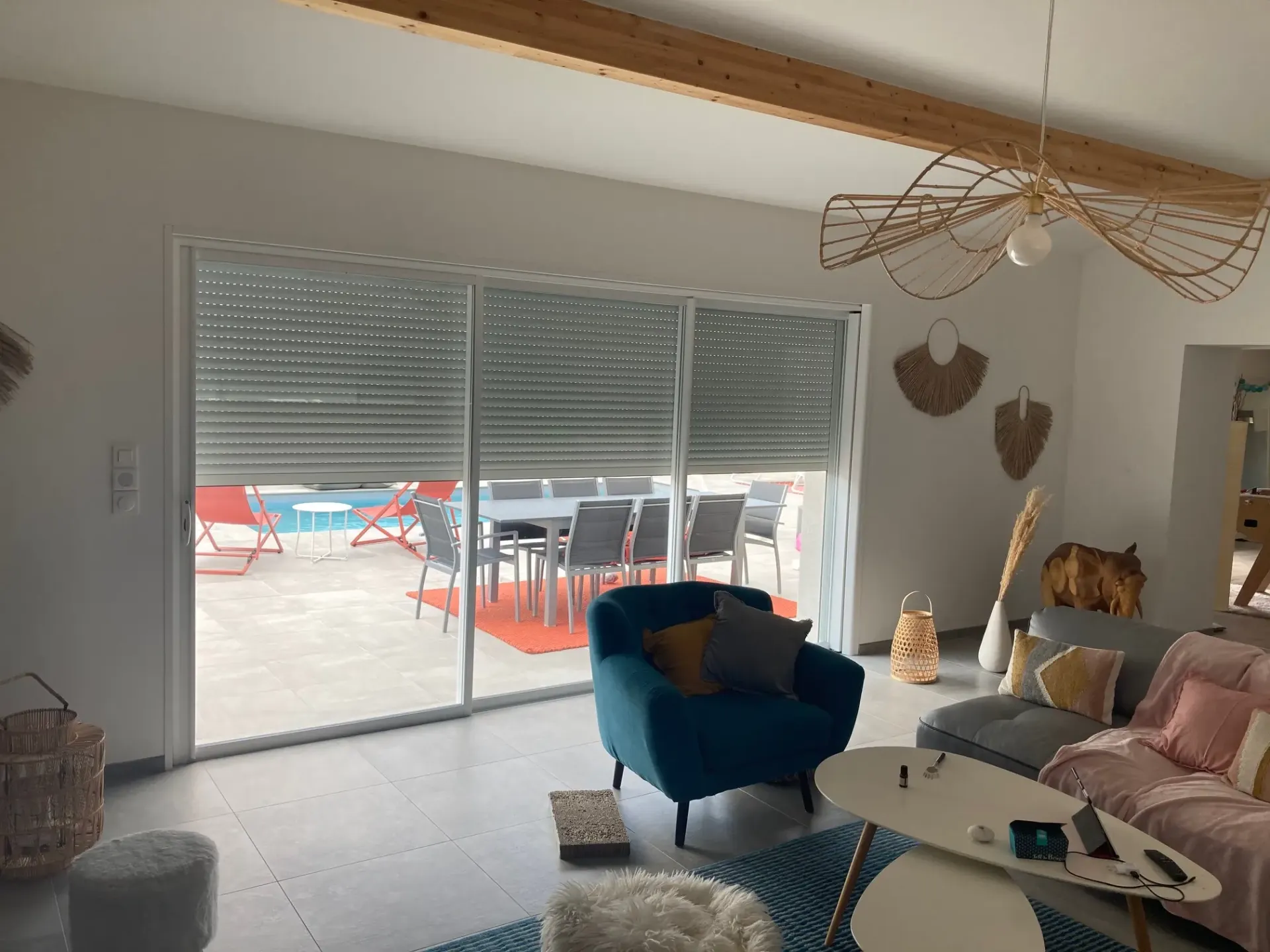 Baie vitrée coulissante avec volet roulant partiellement baissé, donnant sur une terrasse et une piscine