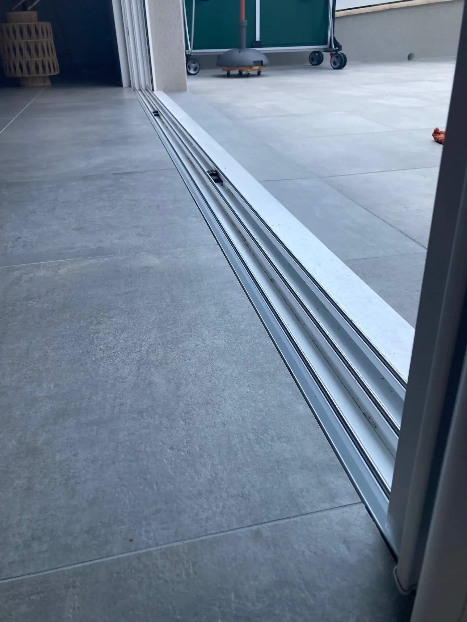 Rail inférieur en aluminium d'une baie coulissante, entre le carrelage intérieur et la terrasse
