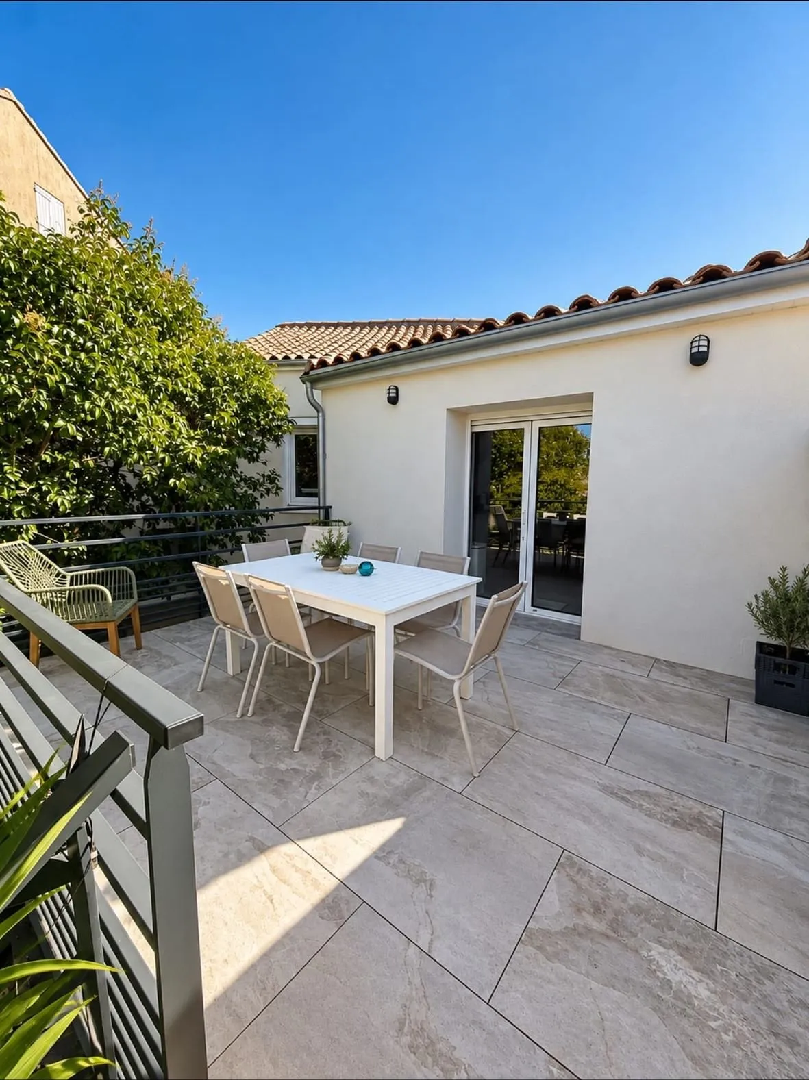 Terrasse en dalles grand format beige avec table et chaises, devant une maison à tuiles