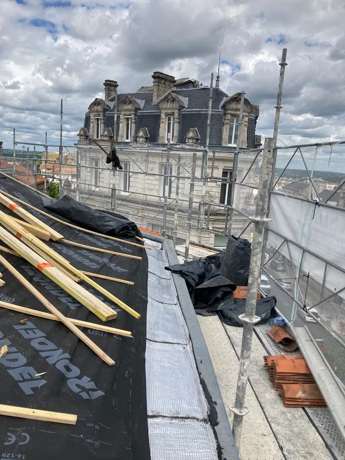 Toit en cours de travaux : écran de sous-toiture noir, liteaux et échafaudage devant un bâtiment à lucarnes